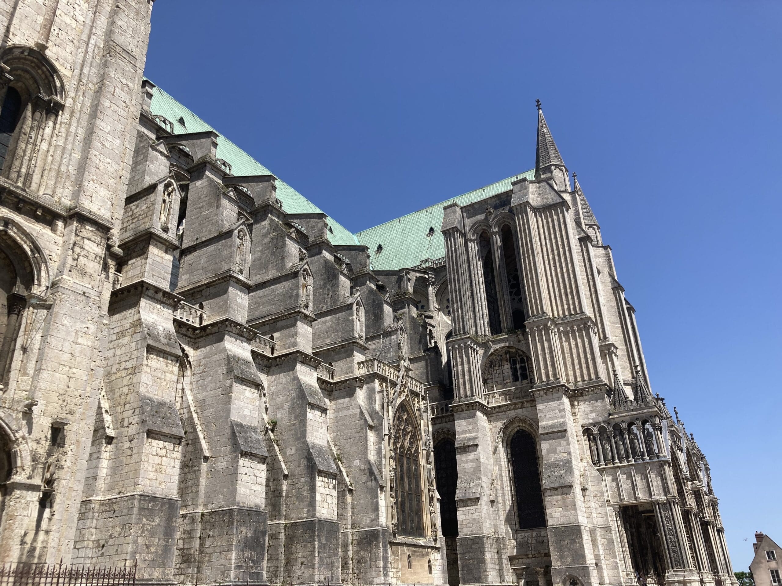 A large Gothic cathedral with detailed stone architecture, pointed arches, and tall stained glass windows under a clear blue sky.