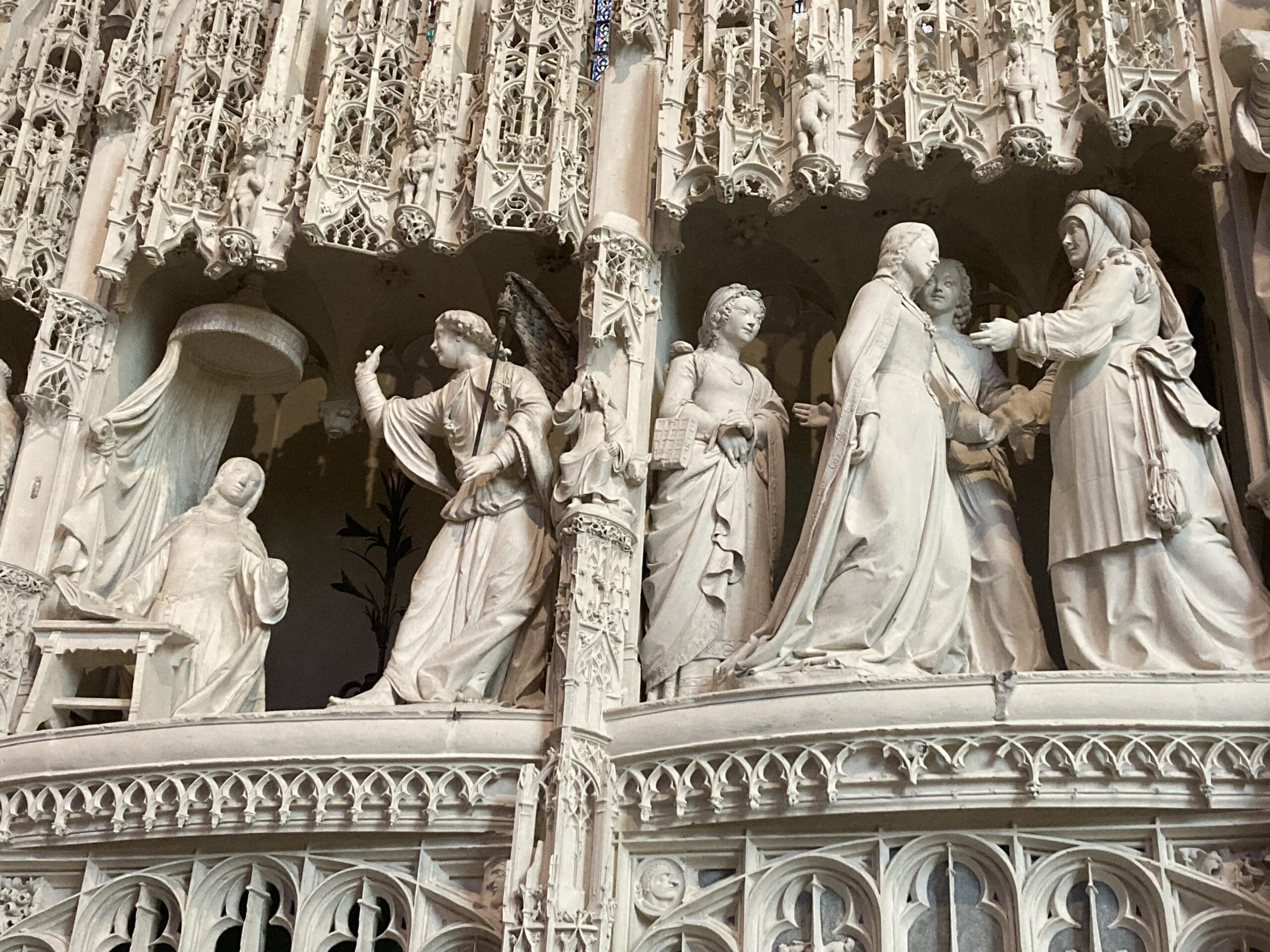 Intricate stone carvings depict angelic and human figures in flowing robes, engaging in various gestures, on an ornate, detailed architectural structure.