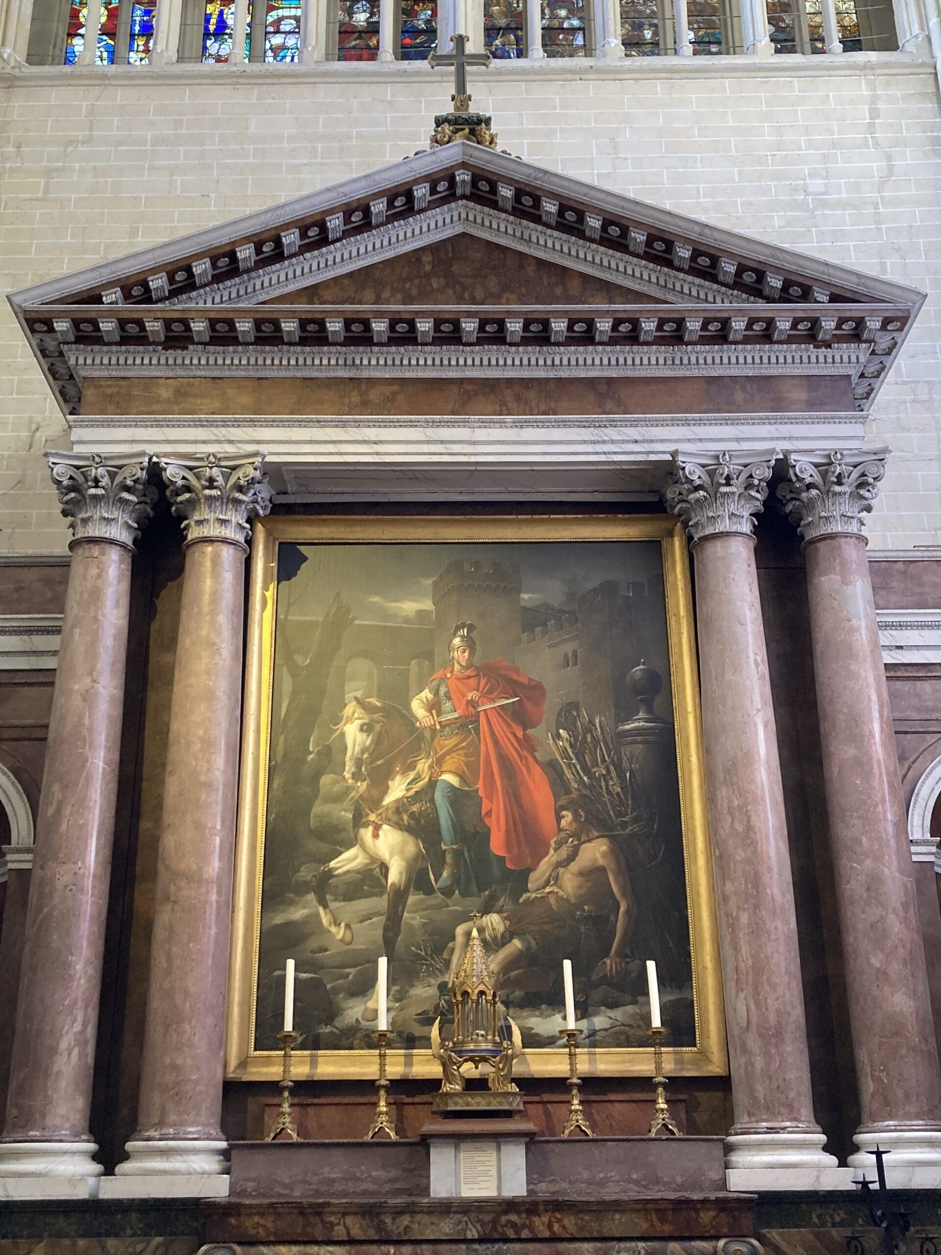 Large framed painting of a man in a red cloak on horseback, displayed on an ornate marble altar with columns, candles, and decorative gold elements beneath a triangular pediment.