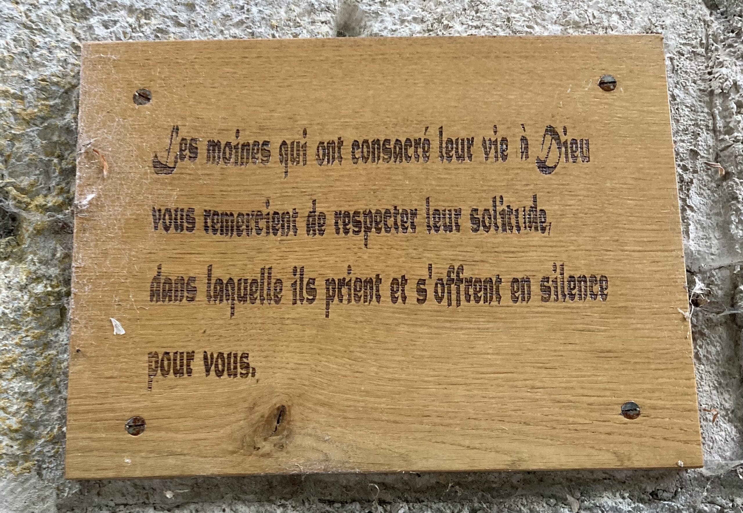 Wooden sign in French asking visitors to respect the solitude of monks, who dedicate their lives to God, pray, and offer themselves in silence for others.