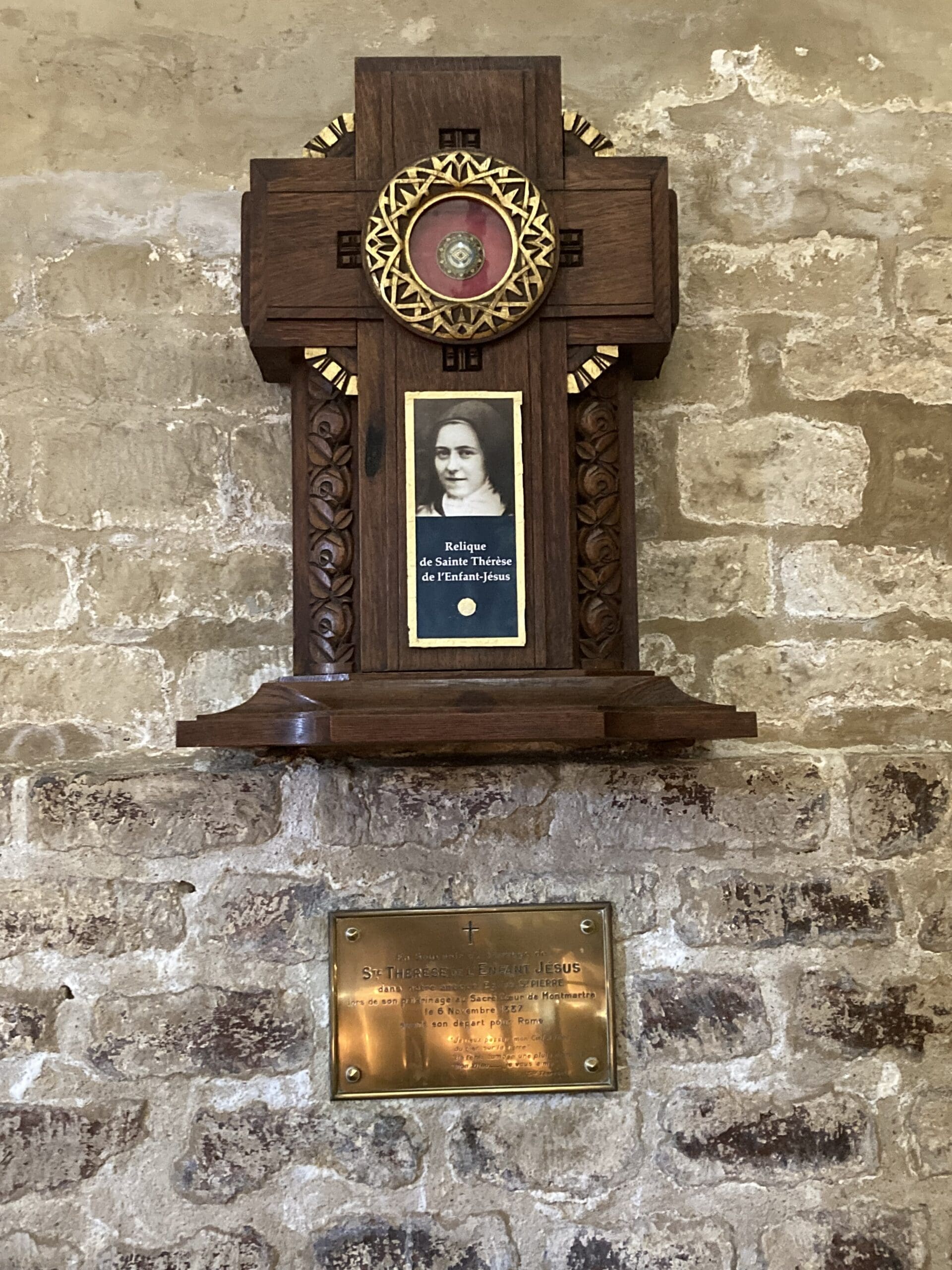 A wooden shrine with a photo of a woman, a red relic, and a gold plaque below, mounted on a stone wall.