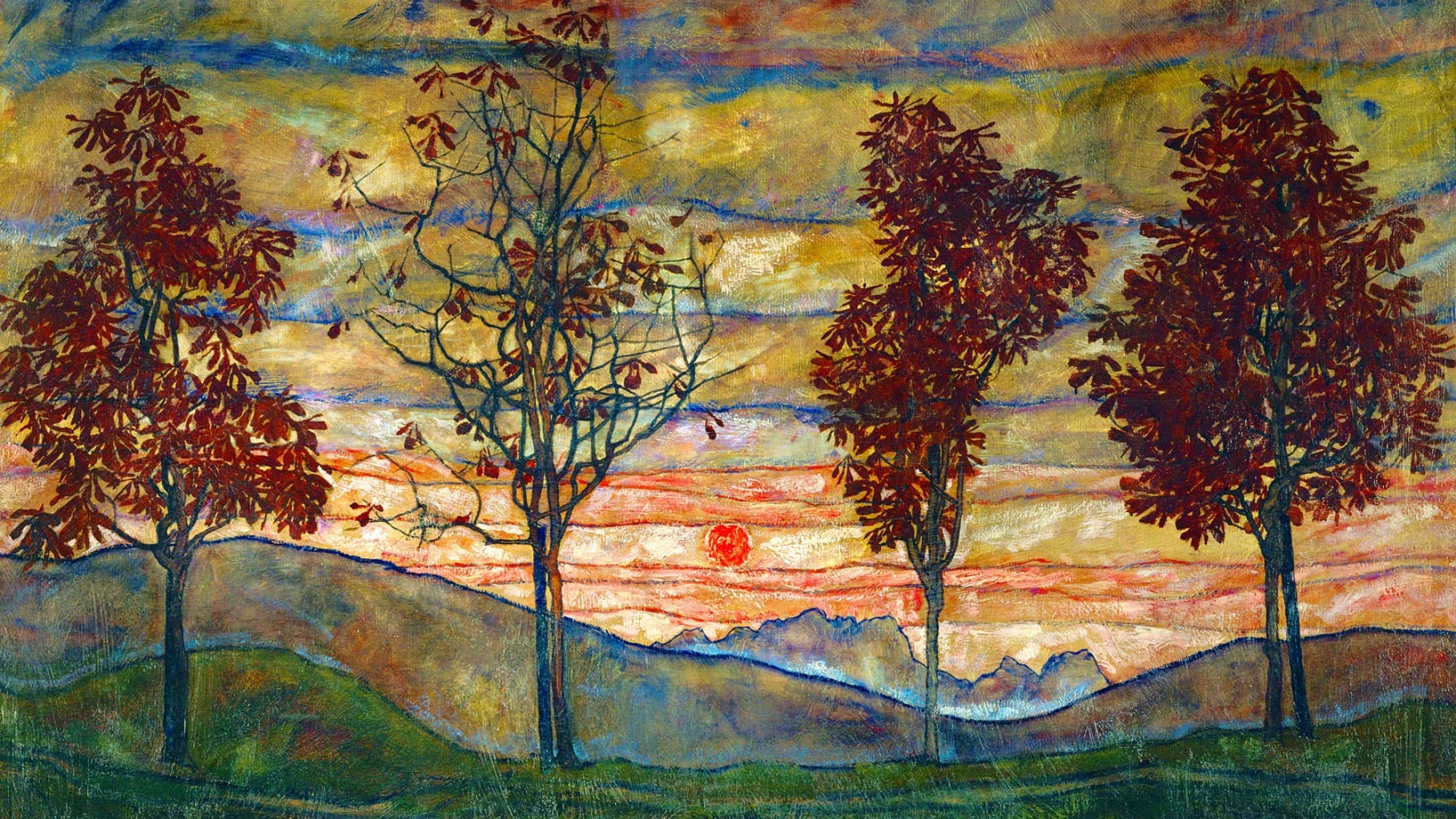 Four autumn trees stand in a row on a grassy hill at sunset, with red and orange leaves, a glowing sun near the horizon, and distant blue mountains under a streaked sky.