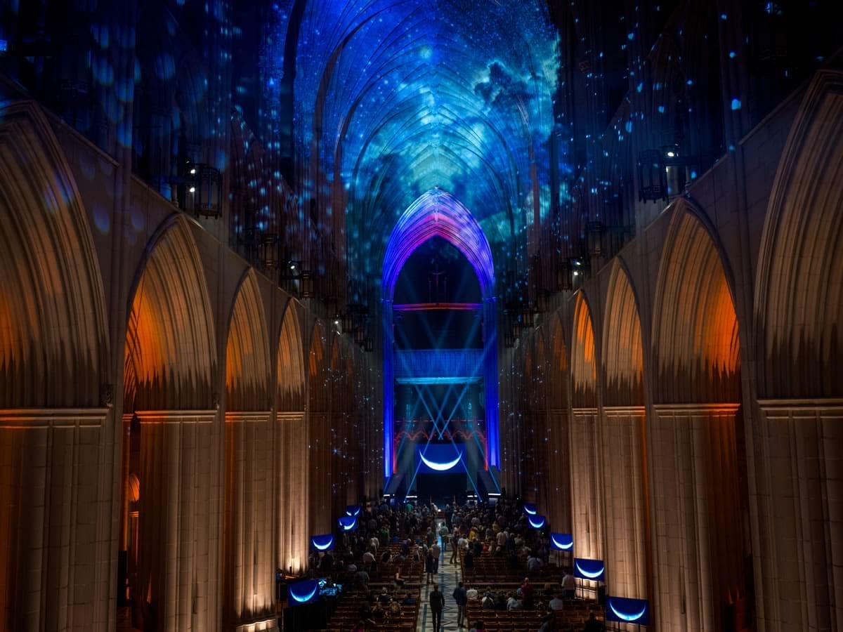 The Cathedral interior bathed in a deep blue projection of stars and clouds across the vaulted ceiling, with the congregation seated below.