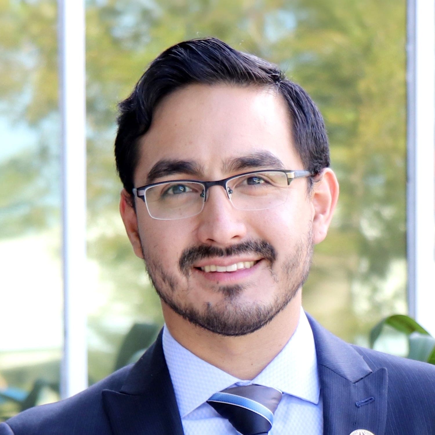 Headshot of a smiling man with a beard and glasses, wearing a suit and tie.