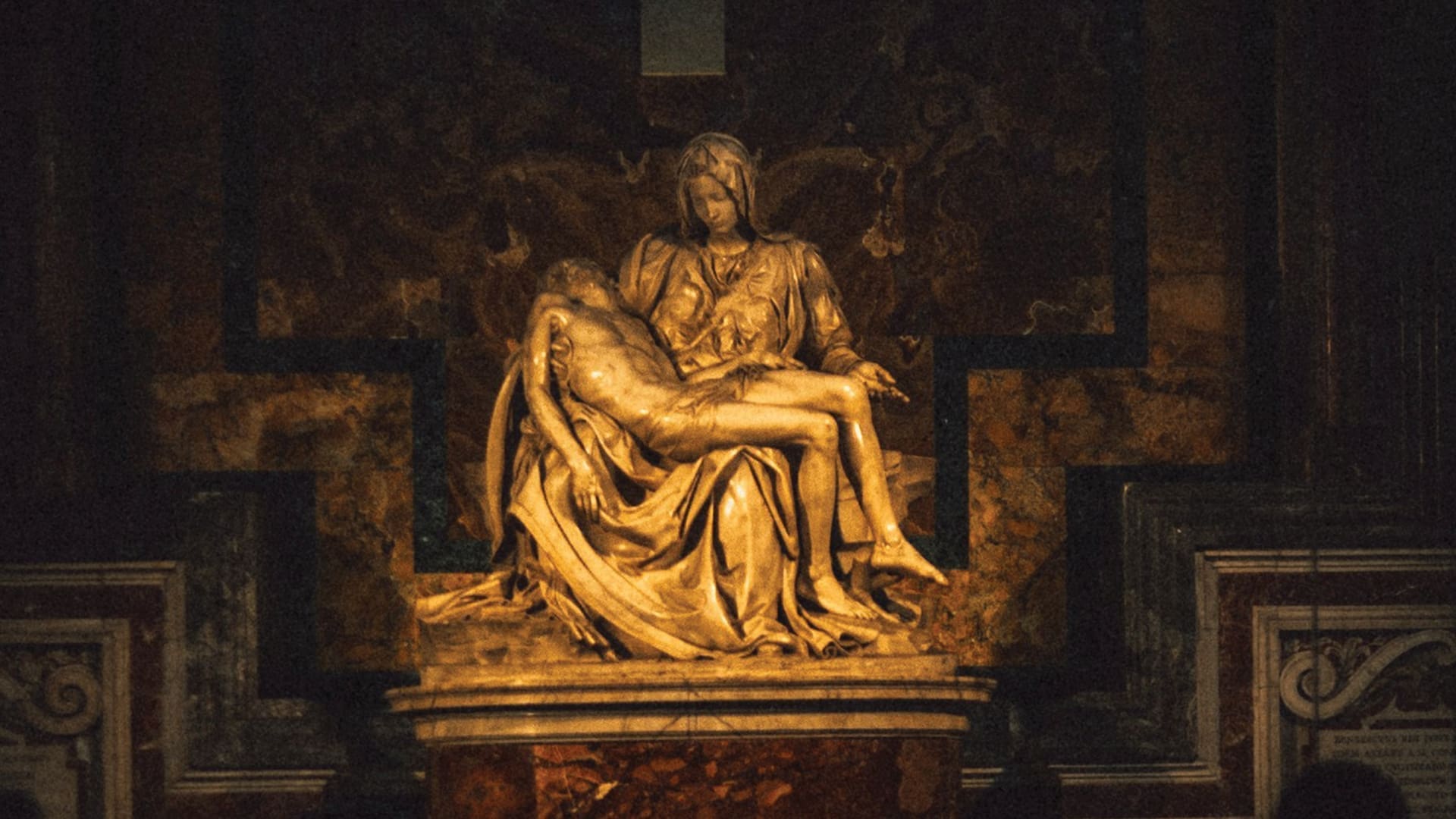 A marble statue depicts a seated woman cradling the lifeless body of a man in her lap, set against a dark, ornate background with rich colors and decorative patterns.